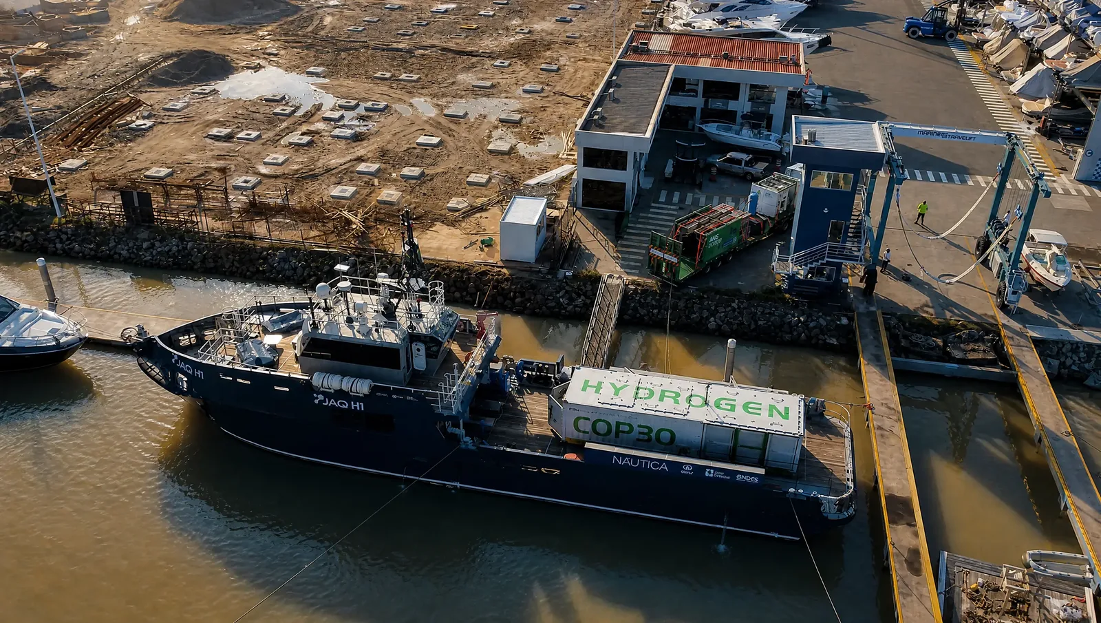 Vista aérea do JAQ H1 atracado na Marina de Itajaí ao lado do Centro de Serviços, com o contêiner "Hydrogen COP30" a bordo e a unidade móvel da AHS Energia na doca